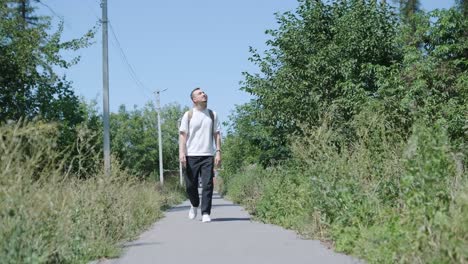 young man walking with guitar on street near forest