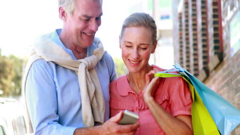 Happy-couple-looking-at-smartphone-together-on-shopping-trip