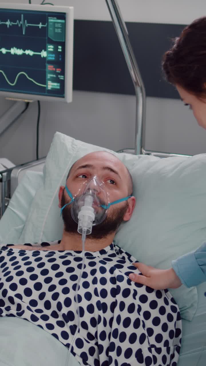 Vertical video: Sick man resting in bed while woman medic putting oxygen mask