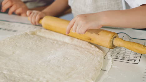 una niña pequeña en la cocina prepara la masa, rodando