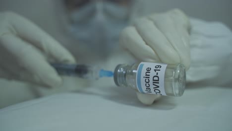 human wearing protective ppe kit carefully initiating to draw out covid 19 vaccine from vial into syringe in horizontal position