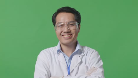 close up of asian man scientist smiling and crossing his arms while standing on the green screen background in the laboratory