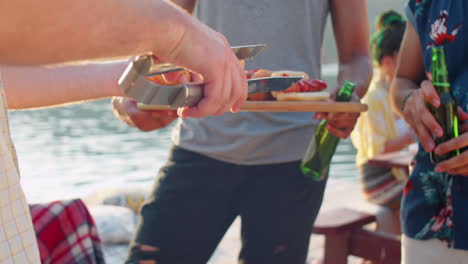 friends making hot dogs with bbq sausages on lake party