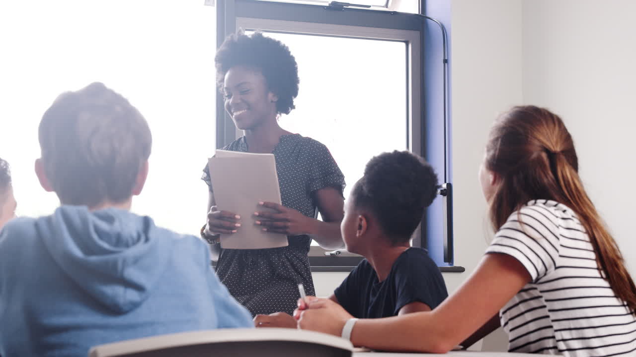 Female High School Tutor Asking Pupils Sitting Around Table Question To which They Raise Their Hands