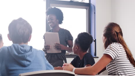 tutora de escuela secundaria preguntando a los alumnos sentados alrededor de la mesa la pregunta a la que levantan las manos