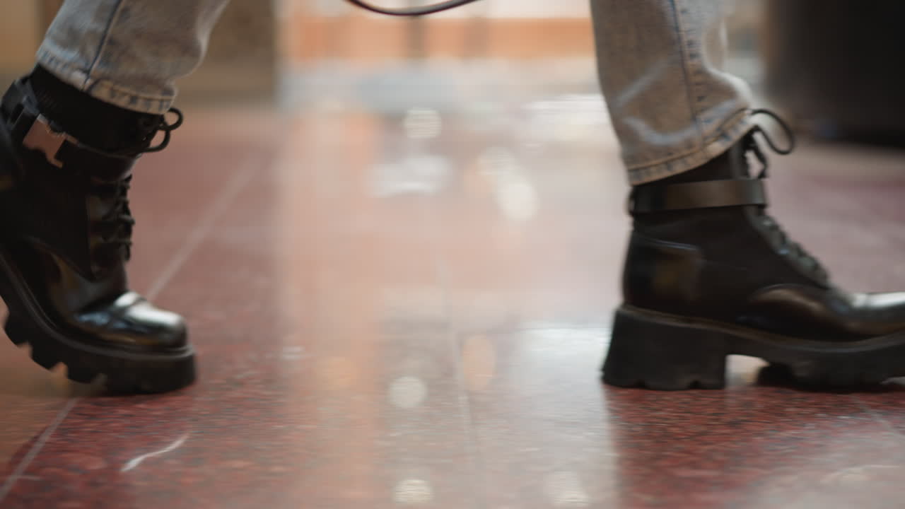 close up leg view of female figure wearing chunky black heel boots striding across glossy tiled floor under bright overhead lights in modern mall interior capturing motion and style