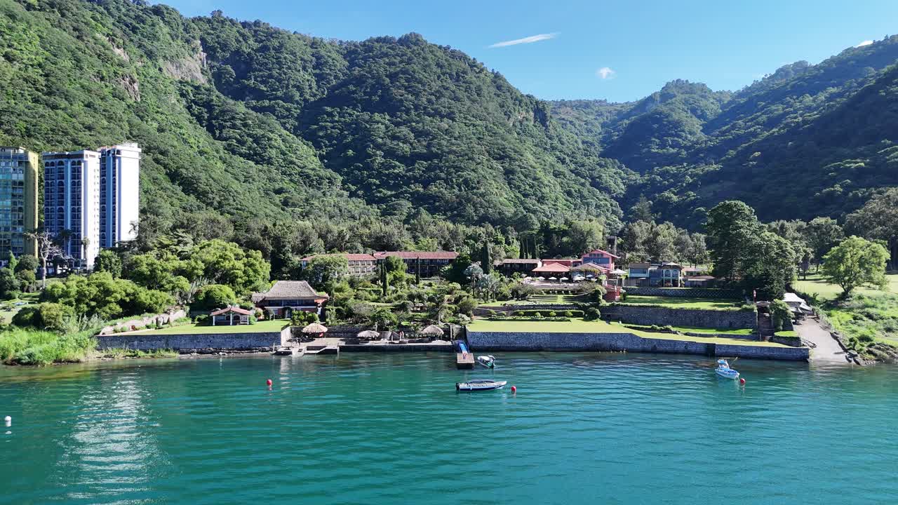 Drone flies from hotel on Lake Atitlán, showcasing buildings, boats and the coastline.