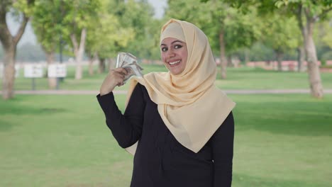 happy muslim woman using money as fan in park