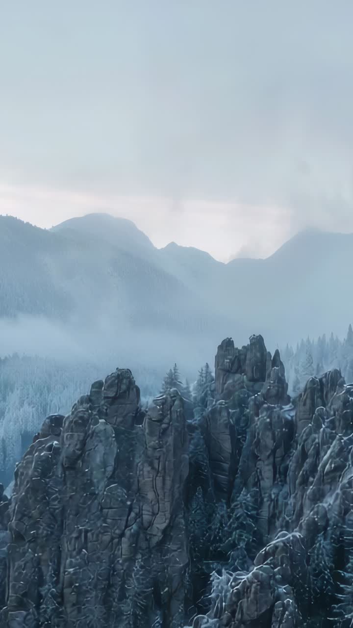 Vertical video: Nudging moving mist from pale light showing far peaks, jagged spires, snowy trees