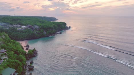 Drone-flying-over-cliffs-and-turquoise-ocean-towards-the-pink-sunset-at-Uluwatu