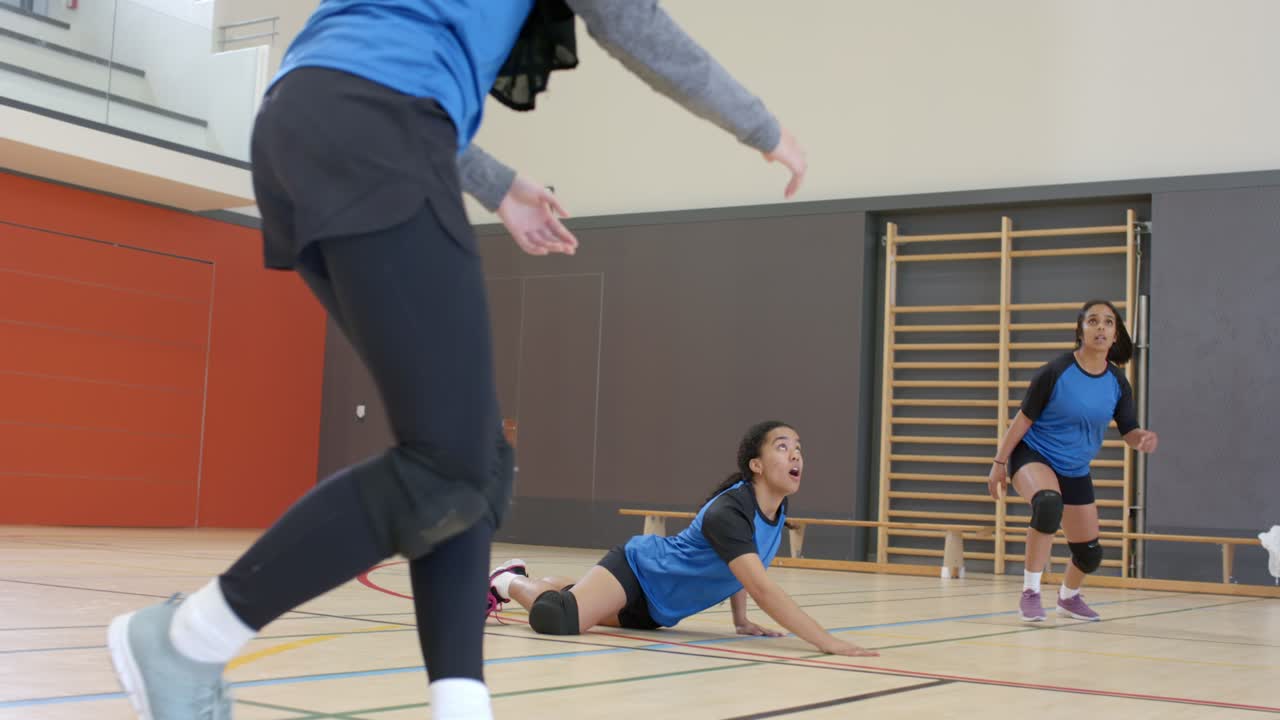 Diverse compagne di squadra di pallavolo anticipano la palla, si lanciano e fanno un bagher su un campo in legno.