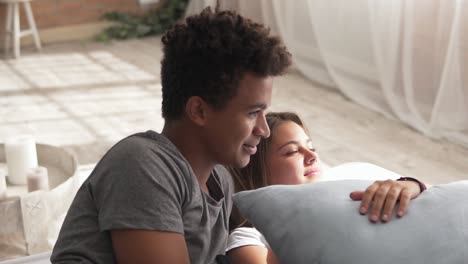 young cute multi ethnic couple lying in bed and talking. handsome african man is telling something. lovely man and woman in love