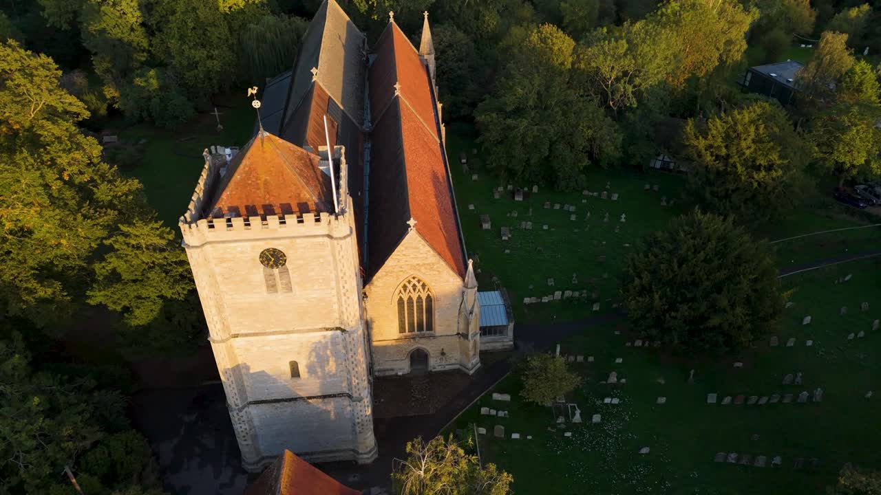 Aerial drone orbit of Dorchester Abbey in Oxfordshire, England. The shot begins to the right of the abbey frontage, moving left while rising, and ends with a top-down view of the medieval stone roof
