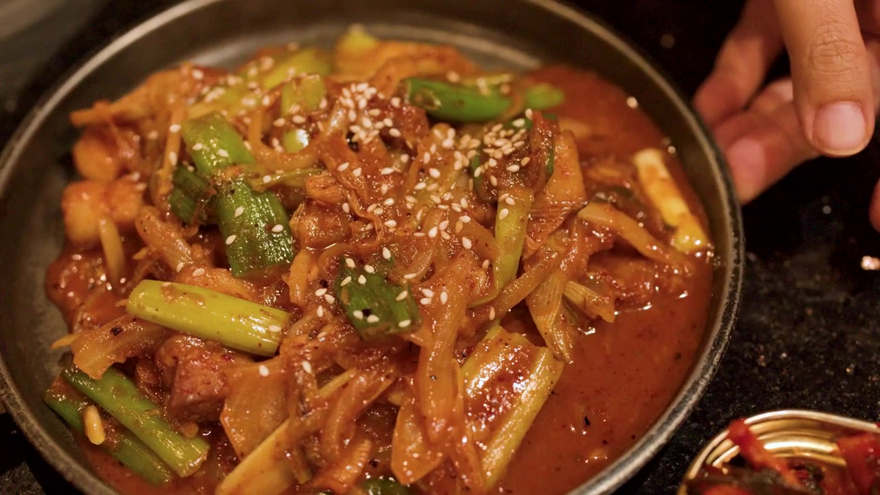 ภาพระยะใกล้แบบนิ่งของทักคาลบีหมูรสเผ็ดพร้อมต้นหอมและงาในร้านอาหาร