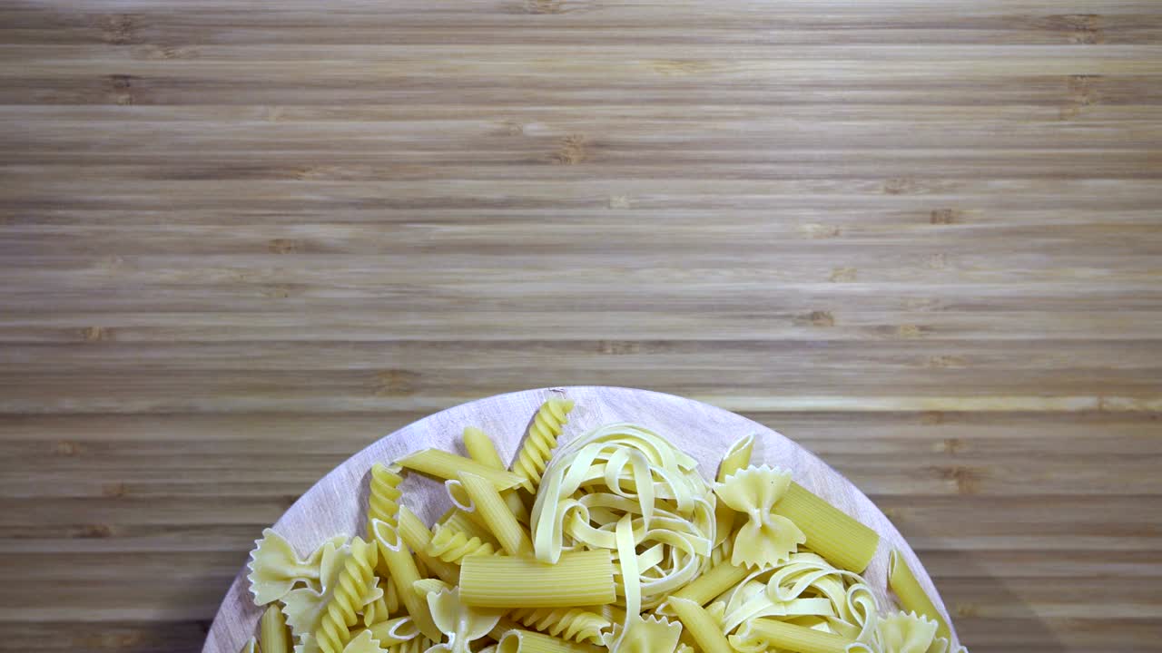 varias pastas crudas girando en una tabla de cortar en blanco, bucle