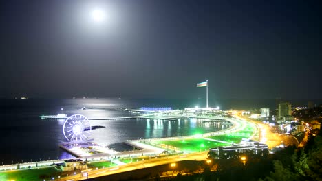 top view of a big city at night, ferris wheel on the background of the sea and the lunar path. traffic on the roads. time lapse