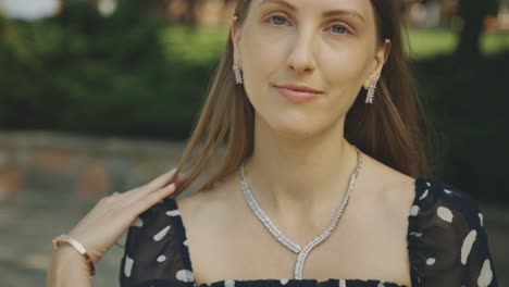 portrait of young adult woman brushing hair with one hand smiling at the camera with opaque nature background - medium closeup slow motion