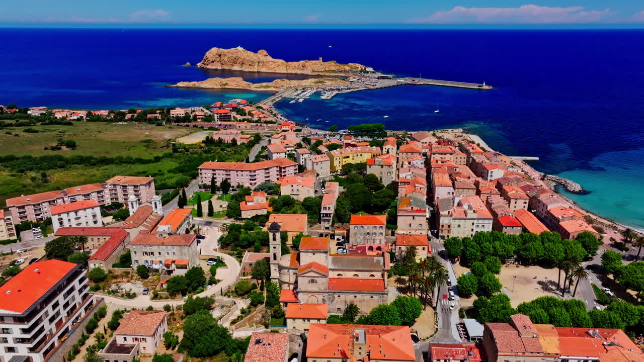 Aerial drone shot over the coastal town Île-Rousse in the Balagne region in Corsica, France. View of the beach and turquoise. Ile de la La Pietra in the background. Summer holidays destination