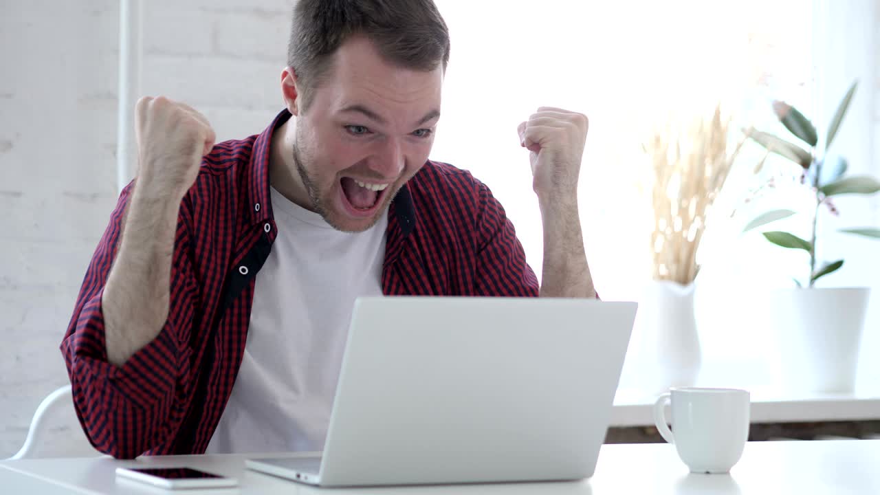 성공을 축하하는 흥분한 젊은이, 노트북에서 일하고