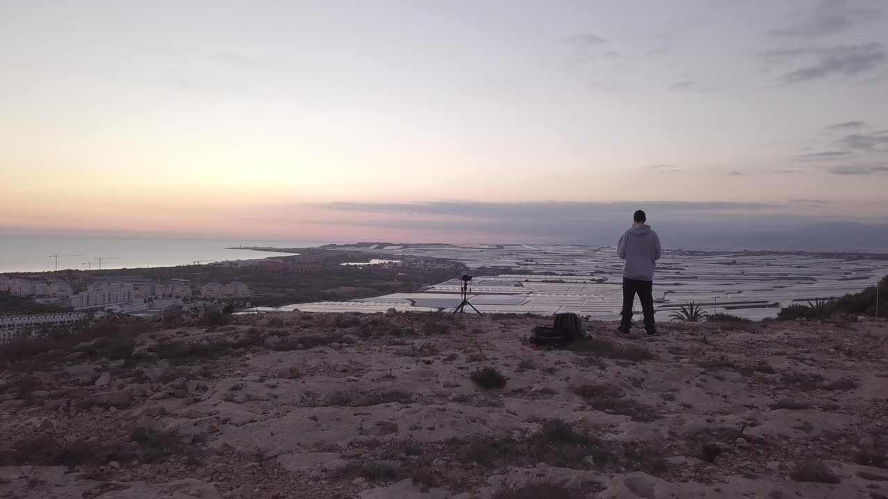 Photographer at Sunrise Over Coastal City and Greenhouses