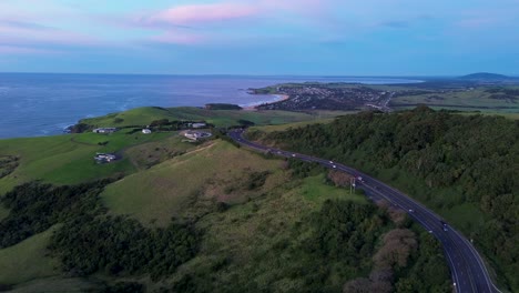 Paisaje-Drone-Aéreo-De-Automóviles-Conduciendo-A-Lo-Largo-De-Princes-Highway-Autopista-Carretera-Promontorio-Costa-Tierras-De-Cultivo-De-Gerringong-Kiama-Costa-Sur-Australia-Viajes-Transporte