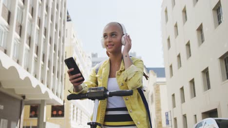 mixed race woman listening music on the street on her e scooter