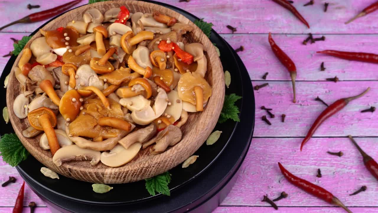 Pickled honey mushrooms sprinkled with allspice peas rotate slowly on turntable red capsicum beside.