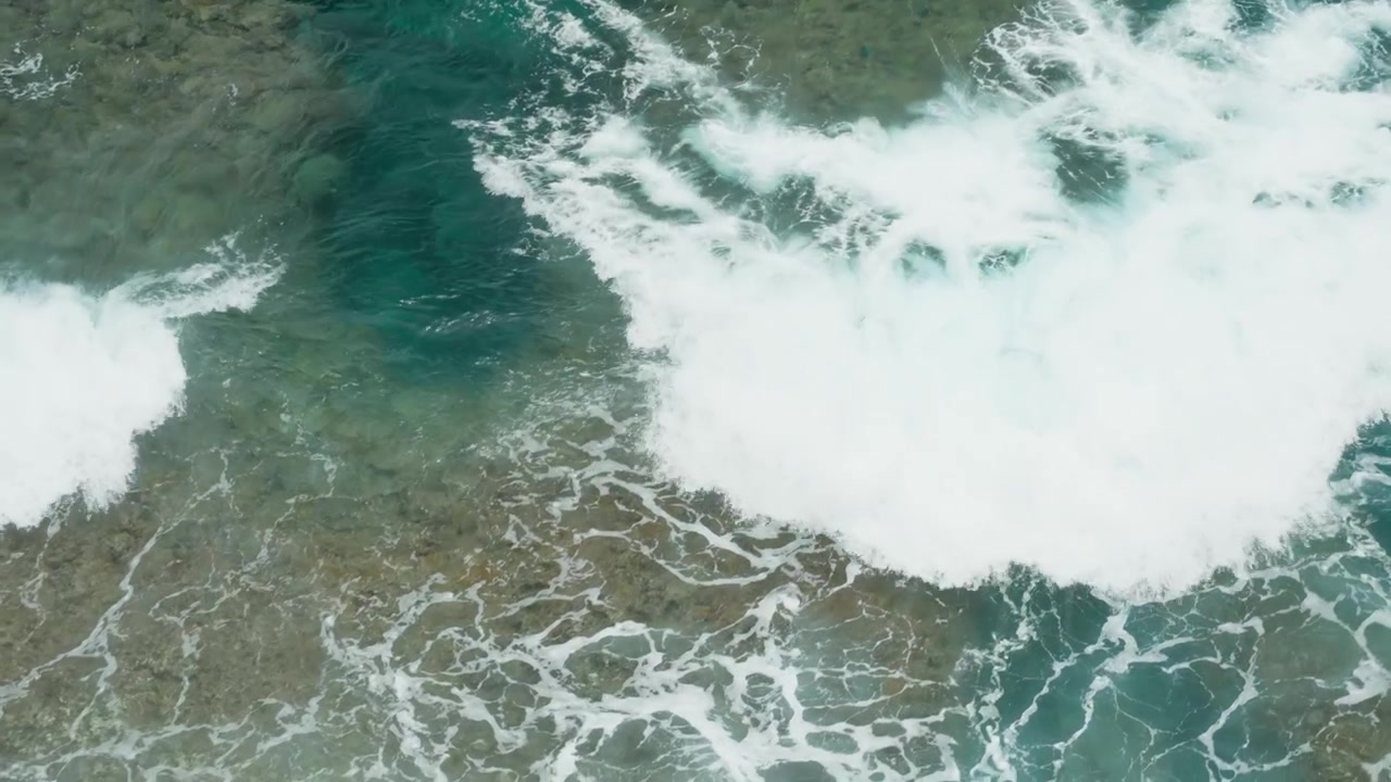 Top view of ocean waves breaking over rocky coastline with turquoise water and white foam