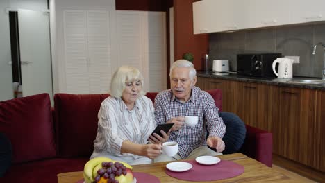 Senior-old-couple-grandparents-talking-and-using-digital-tablet-computer-at-home.-Internet-shopping