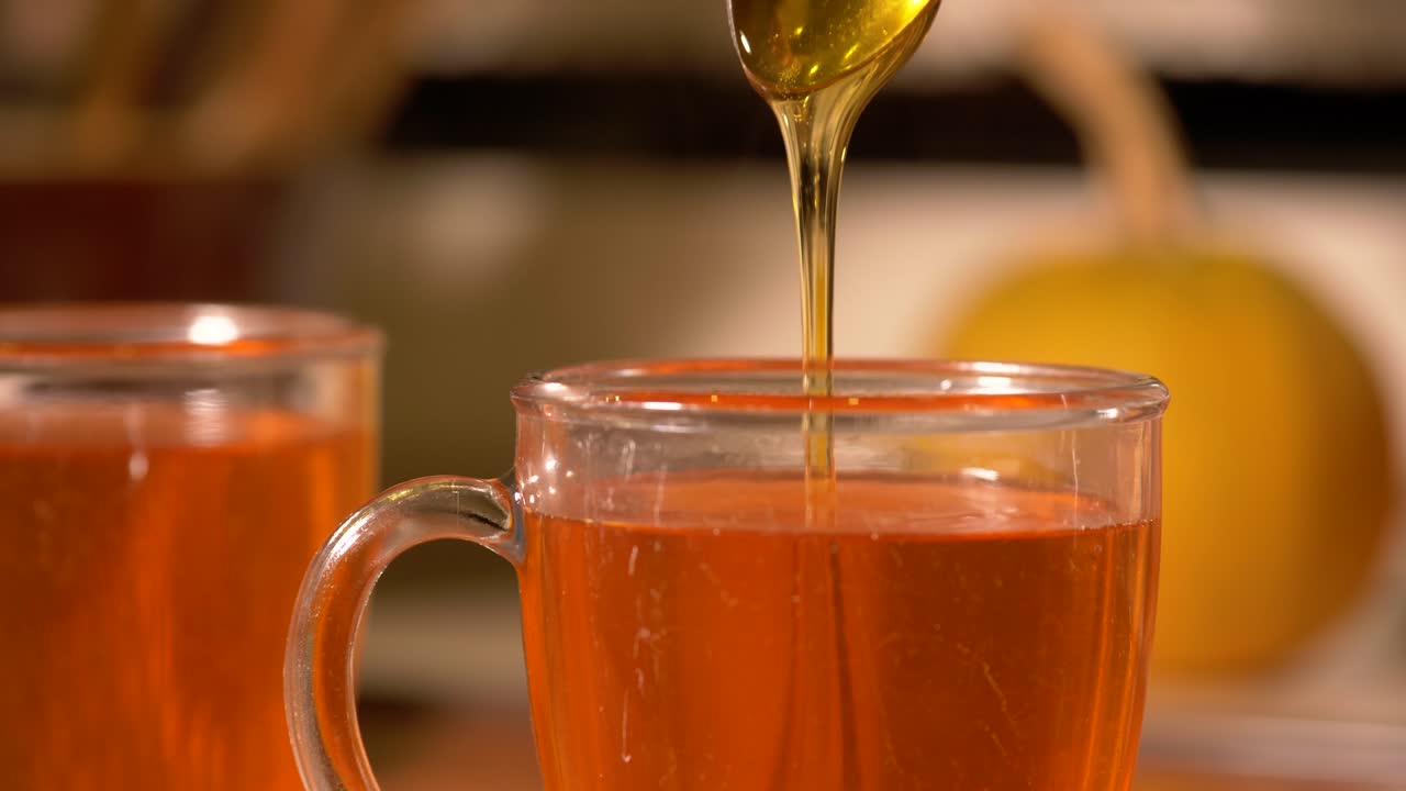 Aggiunta di un cucchiaino di miele dorato in una tazza da tè calda e fumante.