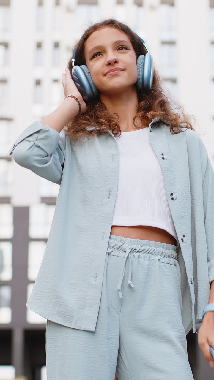 niño preadolescente feliz con auriculares inalámbricos eligiendo escuchar música bailando al aire libre en la calle de la ciudad