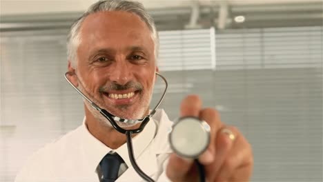 un médico sonriente apuntando con un estetoscopio a la cámara