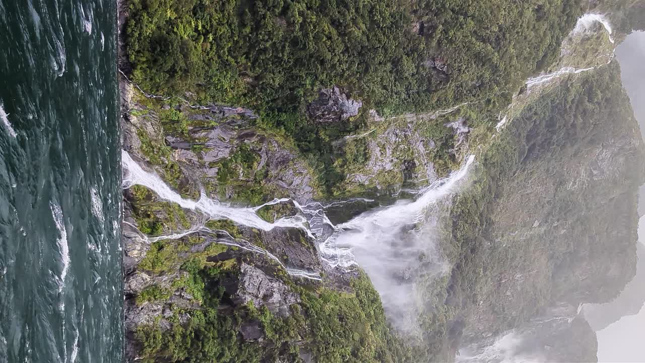tormenta del día del juicio final soplando agua que cae lejos de las montañas en milford sound, vista vertical