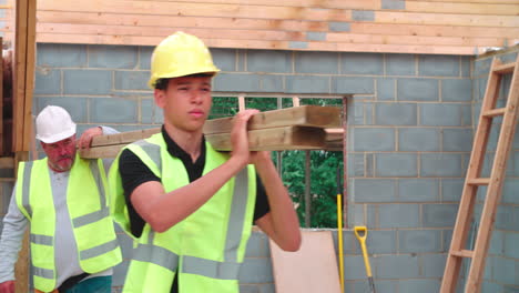 builder and apprentice carrying wood on construction site