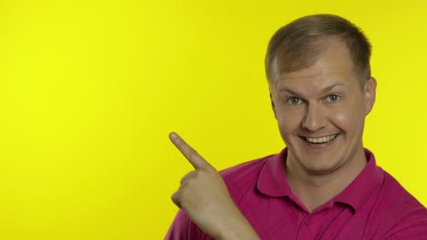 Portrait-of-young-man-posing-in-pink-t-shirt.-Happy-smiling-guy-pointing-at-something-with-hand