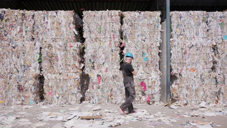 male worker inspects paper bales at recycling facility, wide slomo