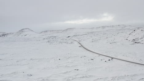 Antena:-Sobre-Un-Paisaje-Blanco-Como-La-Nieve-Con-Carretera,-Montaña-En-Invierno-De-Islandia,-Nevando,-Frío,-ártico