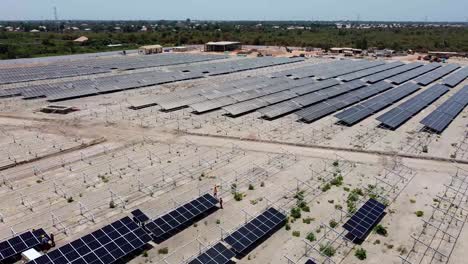 Aerial-rotating-dolly-view-of-technicians-and-engineers-working-installing-bifacial-solar-panels-at-solar-farm-project-site-under-construction-in-Jambur,-Gambia