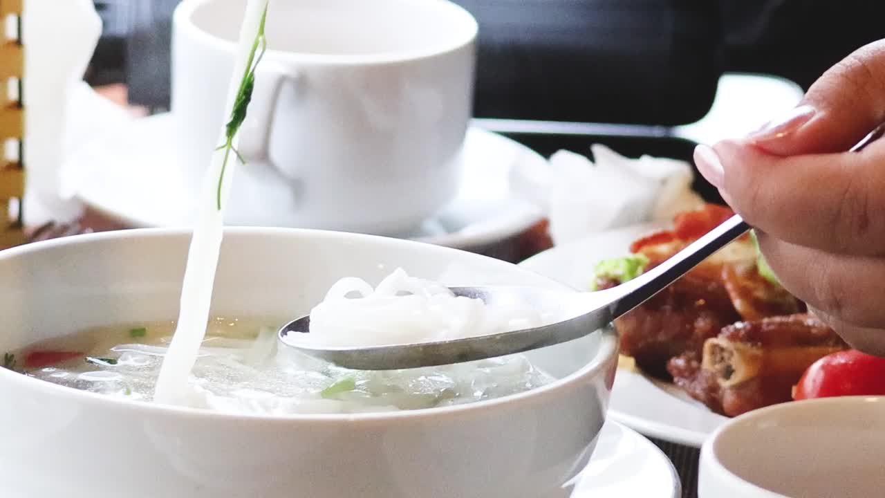 Close-up of using chopsticks to transfer noodles and toppings to a spoon over a soup bowl.