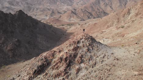 revealing aerial epic shot from drone of an young male standing on top of a rocky mountain in hatta, united arab emirates