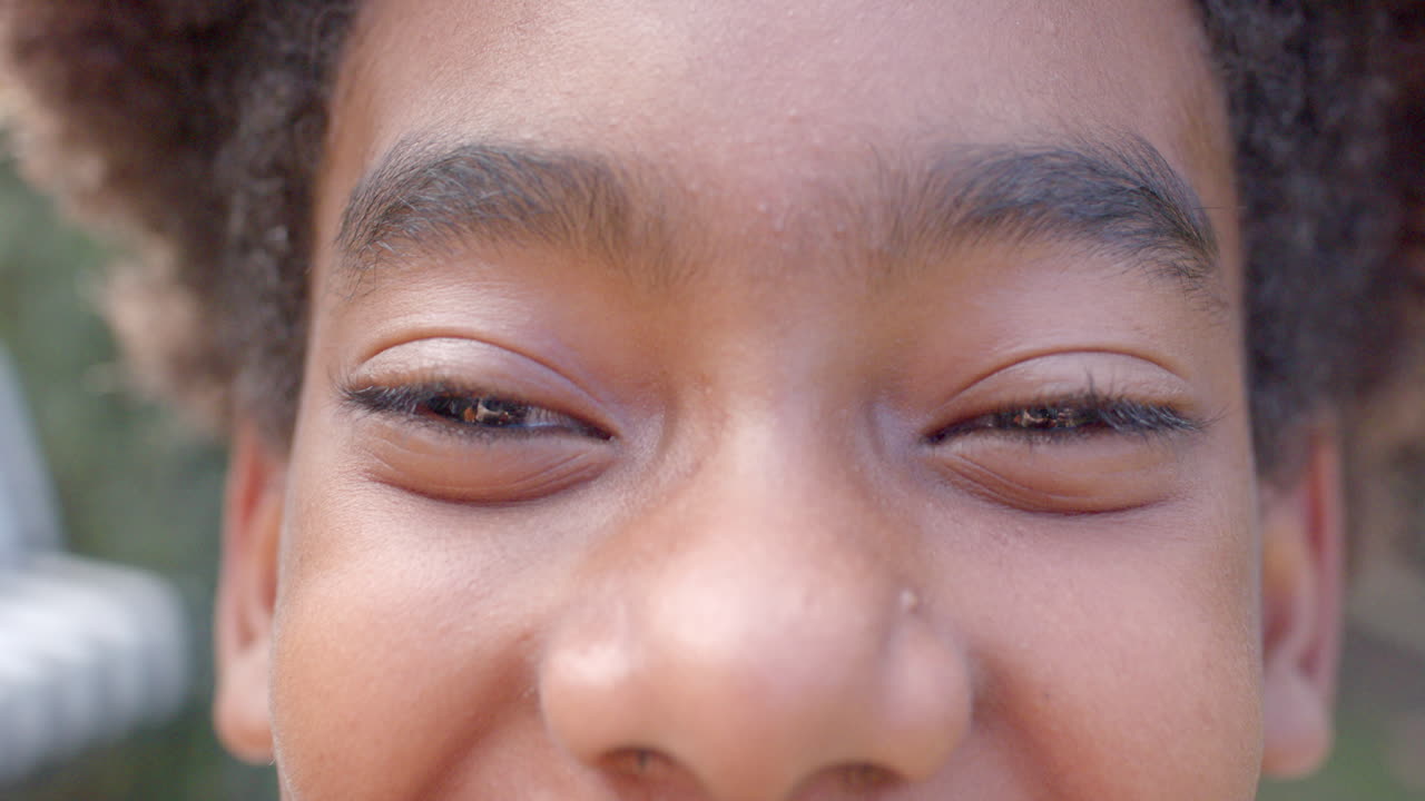 Portrait of happy african american boy looking at camera, smiling in garden, slow motion