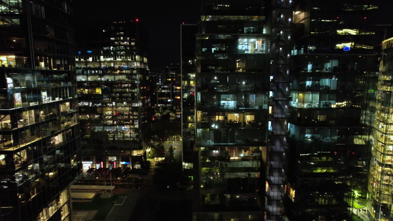 dolly aéreo lateralmente a lo largo de nueva las condes edificios modernos con luces encendidas por la noche, santiago chile