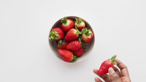 hand picking strawberries from a bowl