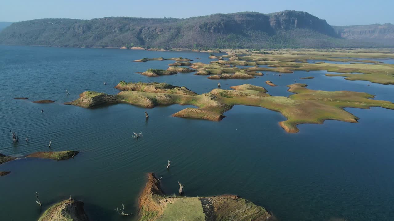 Aerial view of the peaceful surroundings of Karamchat Dam, with distant hills and lush green vegetation.