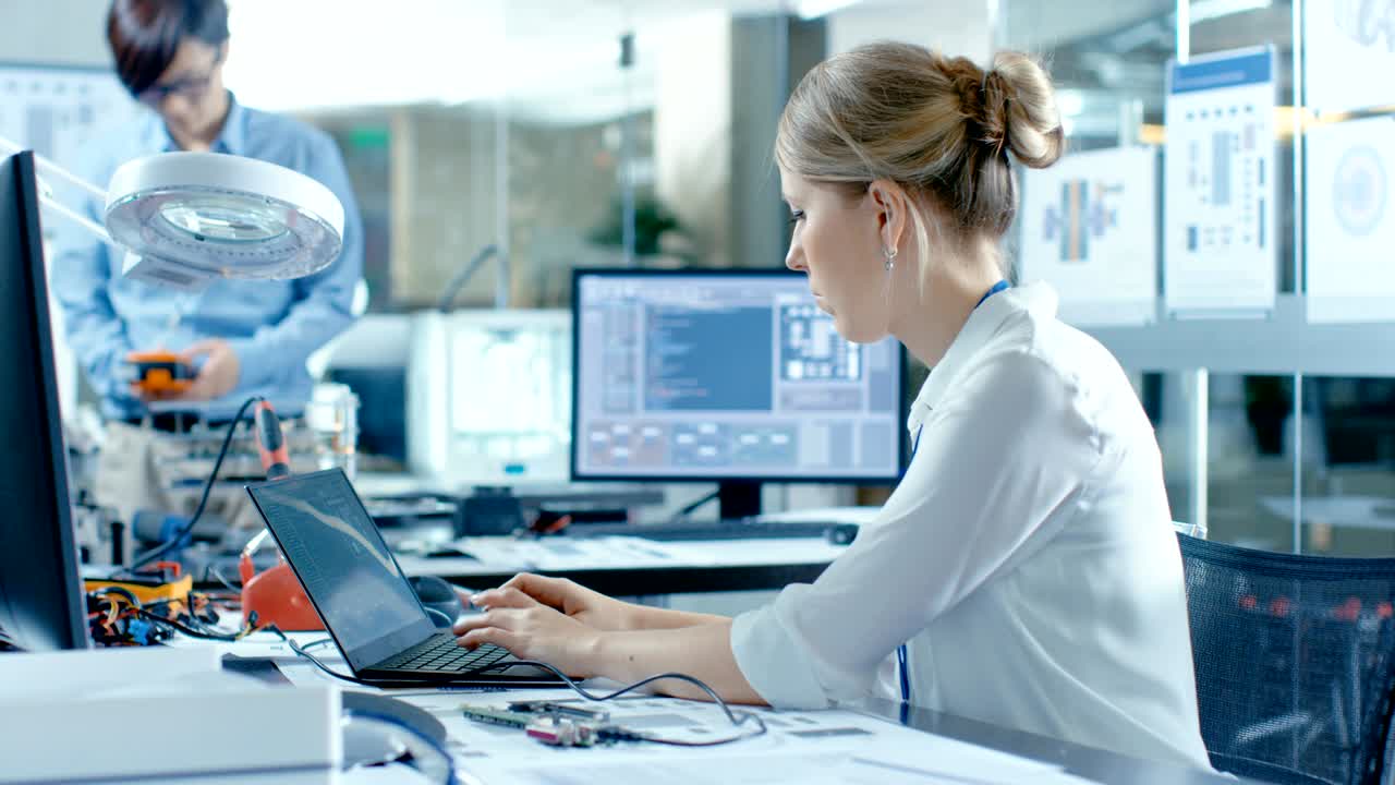 científicas informáticas conectan una placa de circuito a su portátil con una pantalla verde simulada. ella trabaja en el laboratorio tecnológicamente avanzado.