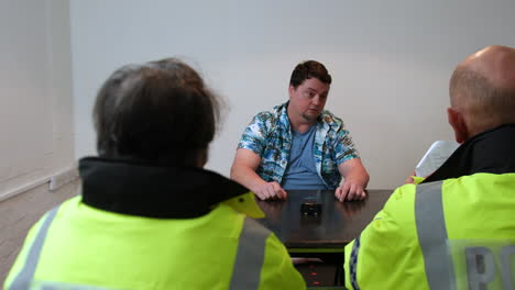 two police officers are interviewing a mature man in the station interrogation room