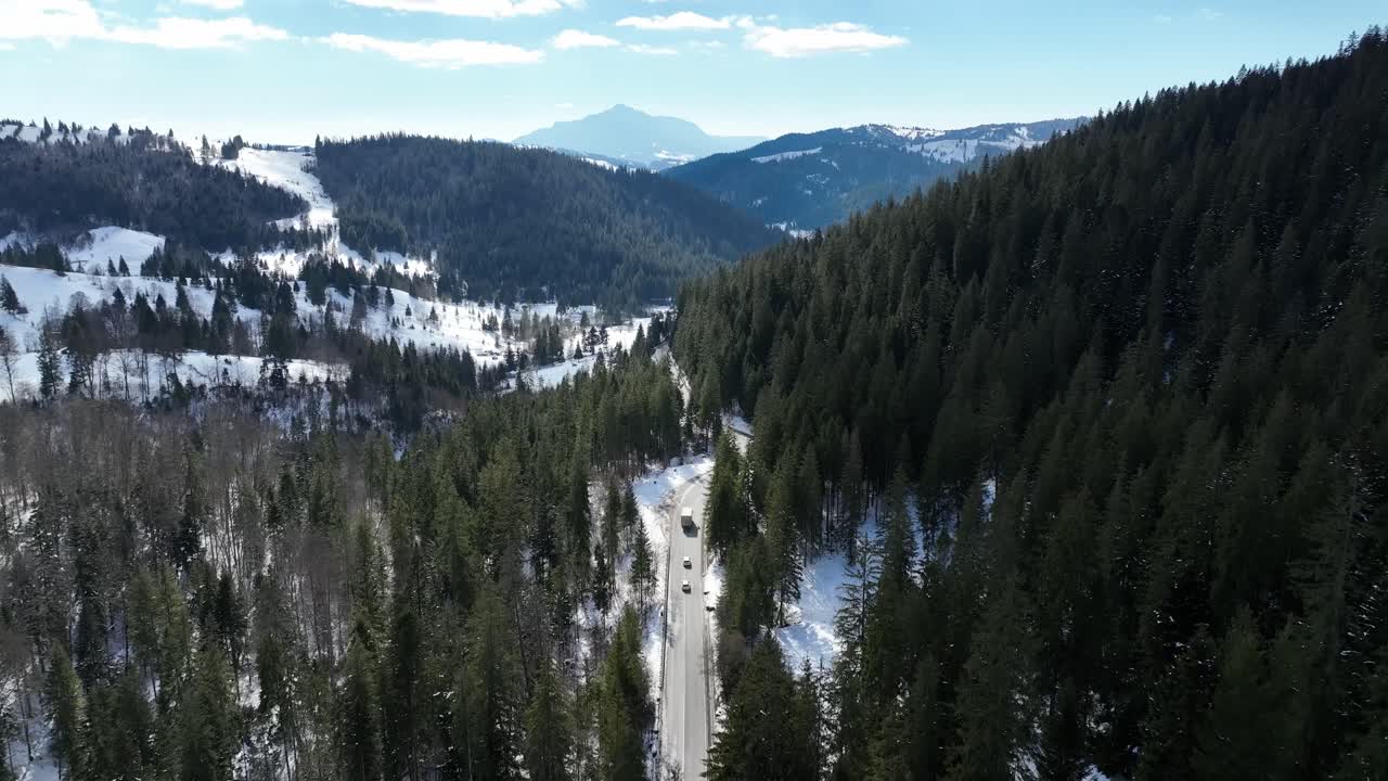 un camino de montaña nevado rodeado de densos bosques de hoja perenne, vista aérea