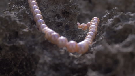 cinematic shot of a pearl necklace laying on marine rock on a beach, 120 fps, slomo