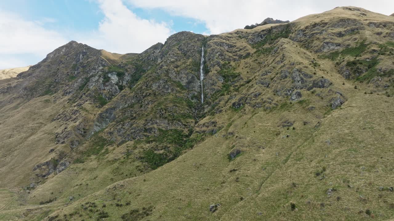 Scenic aerial drone view of narrow waterfall in wild, rugged and rocky landscape in the outdoor mountainous wilderness of New Zealand Aotearoa