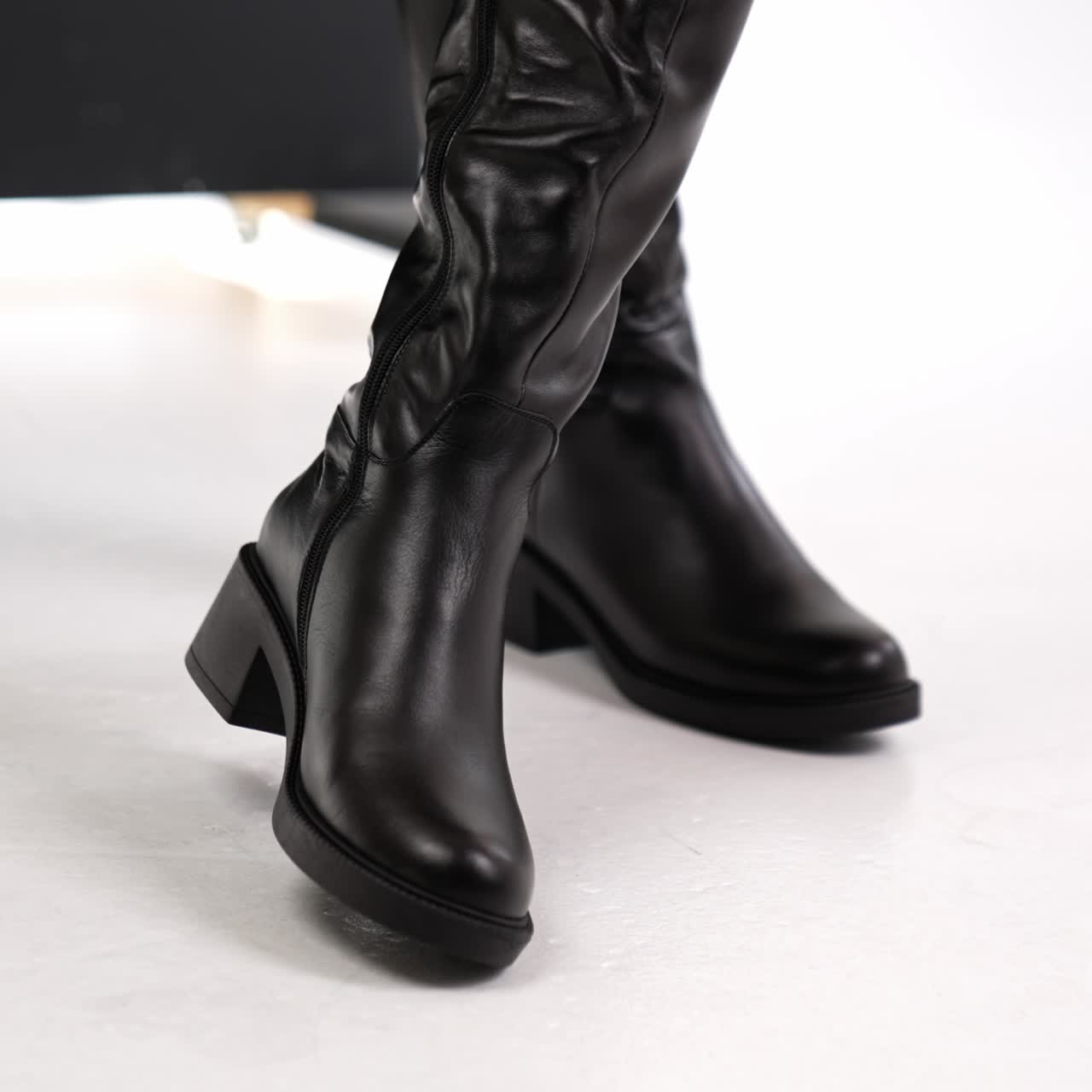 Beautiful elegant stylish female boots presentation. Lady turning and showing fashionable footwear at white floor backdrop. Close up